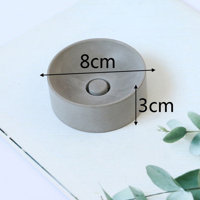May include: A gray concrete ring dish with a diameter of 8 inches and a height of 3 inches. The dish has a small indentation in the center.