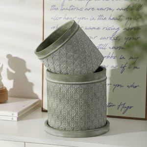 May include: Two stacked green ceramic planters with a decorative embossed pattern. The planters are round in shape and have a slightly flared lip.