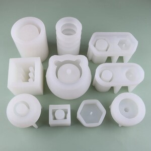 May include: A set of 10 white silicone molds for making concrete planters. The molds are in various shapes, including round, square, hexagonal, and rectangular.