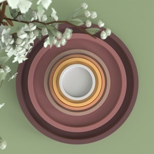 Puede incluir: Un conjunto de cuatro bandejas circulares anidadas en tonos de marrón, naranja y blanco. Las bandejas están dispuestas en un patrón concéntrico, con la bandeja más pequeña en el centro y la bandeja más grande en el exterior. Las bandejas están hechas de un material liso y brillante.