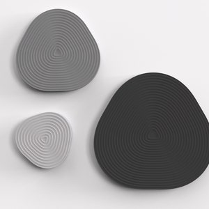 May include: Three wall decor pieces in the shape of a rounded triangle with concentric circles. The largest piece is grey, the medium piece is white, and the smallest piece is black.