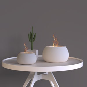 Puede incluir: Dos chimeneas de cerámica blanca con llamas sobre una mesa redonda blanca con una planta de cactus blanca en una maceta blanca.