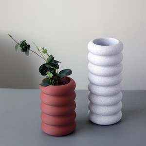 May include: Two ceramic vases with a textured, ribbed design. One vase is a light gray color and the other is a reddish-brown color.