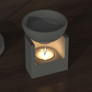 Könnte beinhalten: Ein weißer Keramik-Öldiffusor mit einer kleinen Kerze, die darin brennt. Der Diffusor hat eine runde Oberseite und eine quadratische Basis.