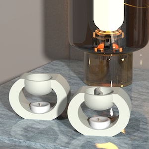 Può includere: Due diffusori di olio in ceramica bianca con una piccola candela in ciascuno. I diffusori hanno una ciotola rotonda al centro e un bordo esterno curvo.