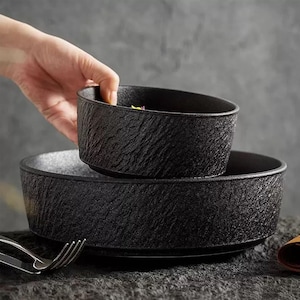May include: Two black ceramic bowls with a textured surface. The smaller bowl is inside the larger bowl.