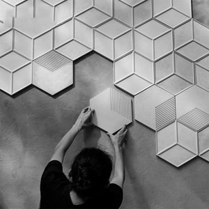 May include: A person is installing white hexagonal tiles with a geometric pattern on a wall. The tiles have a raised, textured surface.