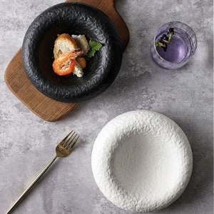 May include: Two ceramic bowls with a textured, crater-like design. One bowl is black and the other is white.