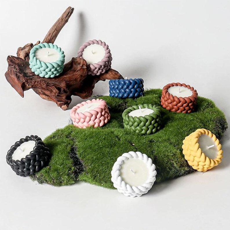 May include: Assortment of eight small, round, decorative candles in various colors, including pink, green, white, yellow, brown, blue, and black. The candles are arranged on a bed of green moss.