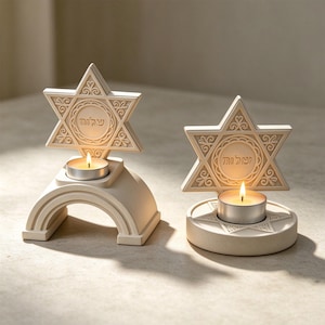 Peut inclure: Deux bougeoirs blanc cassé arborant un motif d'étoile de David avec des volutes complexes et le mot hébreu Shalom inscrit au centre. L'un possède une base arquée, l'autre une base circulaire, tous deux supportant des bougies chauffe-plat allumées.