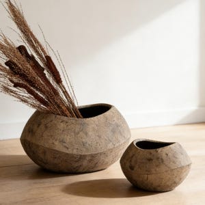 Może przedstawiać: Zestaw trzech ceramicznych kubków z nakrapianym, matowym wykończeniem. Kubki są w odcieniach kremowym, jasnoszarym i ciemnoszarym. Każdy kubek ma prosty, minimalistyczny design, idealny do kawy lub herbaty.