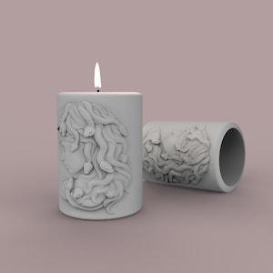 May include: A white candle with a detailed sculpted image of Medusa's face on the side. The candle is lit and the flame is visible.