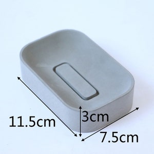 May include: A gray concrete soap dish with a rectangular shape and a raised center section. The dish measures 11.5 inches long, 7.5 inches wide, and 3 inches high.