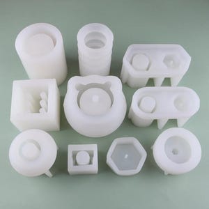 May include: Set of 10 white silicone molds for making concrete planters. The molds are in various shapes, including round, square, rectangular, and hexagonal.