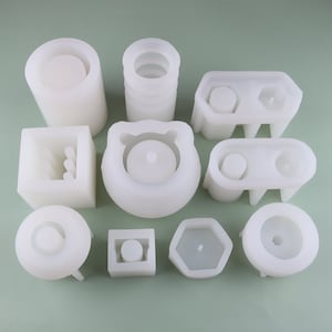 May include: A set of 10 white silicone molds for making concrete planters. The molds are in various shapes, including round, square, hexagonal, and rectangular.
