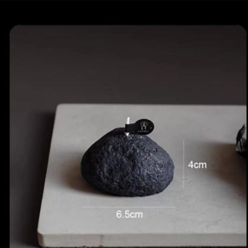 May include: A black stone-shaped candle with a white wick. The candle is 6.5 cm wide and 4 cm tall.