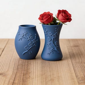 May include: A white ceramic mug with a black handle and the text "But First, Coffee" in a black, bold font. The mug is on a white surface. The mug is approximately 10 cm tall.