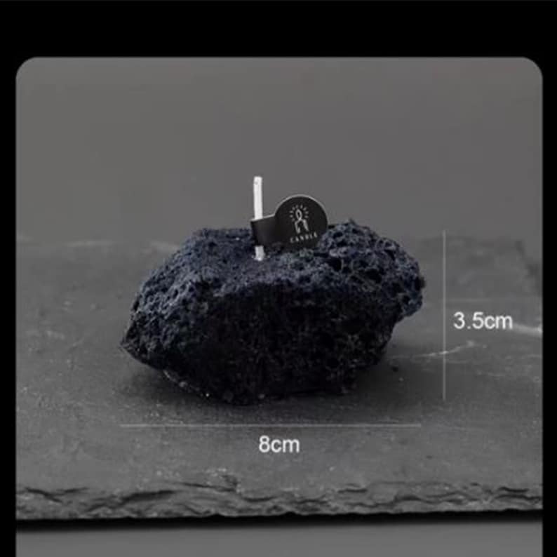 May include: A black lava rock candle holder with a white wick and a small black label that says "Candle". The holder is 8 cm wide and 3.5 cm tall.