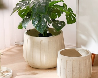 Pode incluir: Dois vasos de cerâmica branca com acabamento texturizado. O vaso maior tem uma planta verde de folhas dentro. Ambos os vasos têm um design canelado.