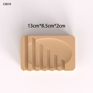 May include: A beige soap dish with a raised oval and ridges. The dish measures 13cm by 8.5cm by 2cm.