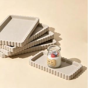 Può includere: Una pila di quattro vassoi rettangolari color beige con bordi smerlati e un vassoio abbinato posizionato davanti. Una piccola candela in vasetto di vetro con un'etichetta che riporta la scritta "Thank you" e un piccolo cuore poggia sul vassoio.