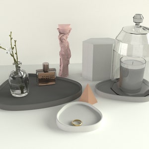 May include: Three grey triangular trays with a variety of items on them, including a glass bottle with a sprig of flowers, a bottle of perfume, a candle in a glass cloche, and a pink statue.