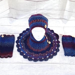 May include: A handmade crochet winter set in shades of blue and burgundy. The set includes a hat, neck warmer, and fingerless gloves, all adorned with wooden buttons. The hat and neck warmer are on a white mannequin head.