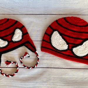 May include: Two red and black crocheted hats with white crocheted eyes. The hat on the left has a long tie.