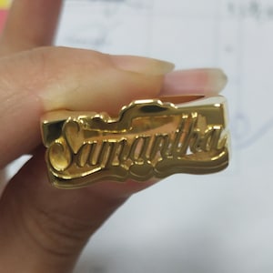 May include: Gold ring with the name Samantha engraved in a cursive font.