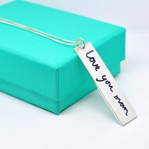 Puede incluir: Un collar de plata con un colgante rectangular que dice "Love you mom" en escritura cursiva.