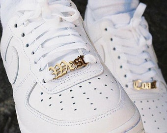 May include: White leather sneakers with gold metal shoe charms that say "West" and "Coast".