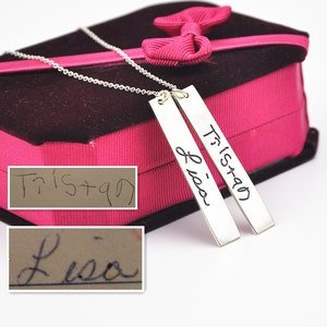 May include: Two silver bar necklaces with the names Tristan and Lisa handwritten on them. The necklaces are in a pink velvet box with a pink ribbon.