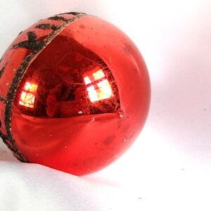 Op de afbeelding: Een rode glazen kerstbal met een zwarte glitterband rond het midden.