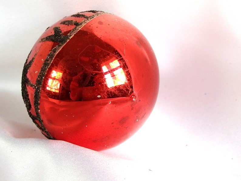 Op de afbeelding: Een rode glazen kerstbal met een zwarte glitterband rond het midden.