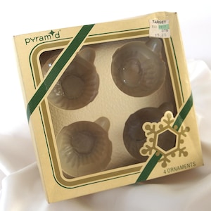 May include: A box of four vintage Christmas ornaments. The ornaments are a light brown color and have a unique, textured design. The box is tan with green and gold accents, and the word "pyramid" is printed on the top.