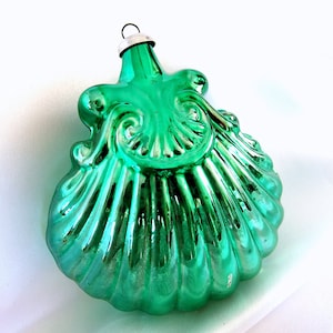 May include: A green glass Christmas ornament shaped like a seashell with a metallic finish.