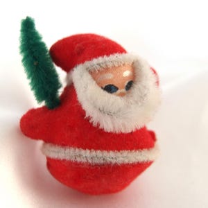 May include: A red felt Santa Claus ornament with a white beard and a green felt Christmas tree attached to his side.