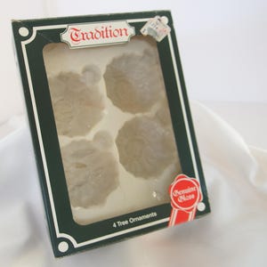 May include: A box of four white glass Christmas tree ornaments with a snowflake design. The box is green and white with the words "Tradition" and "Genuine Glass" printed on it. The box says "4 Tree Ornaments".