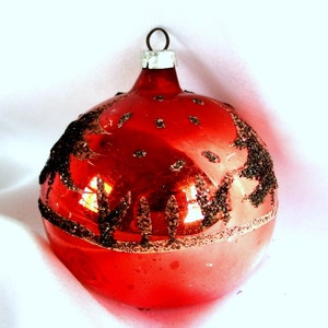 Op de afbeelding: Een rode glazen kerstbal met een zwart glitterontwerp. De bal heeft een zilveren hanger.