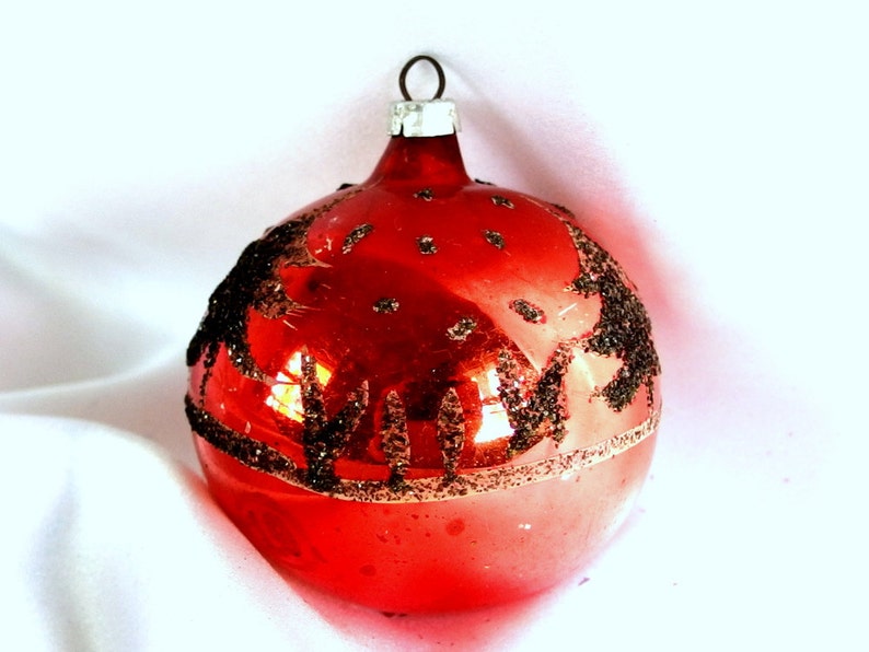 Op de afbeelding: Een rode glazen kerstbal met een zwart glitterontwerp. De bal heeft een zilveren hanger.