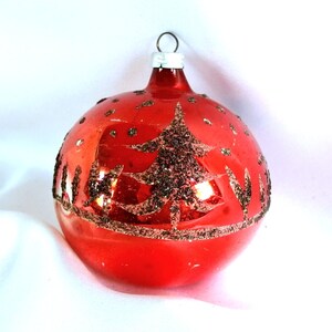 Op de afbeelding: Een rode glazen kerstbal met een gouden glitterboomontwerp.
