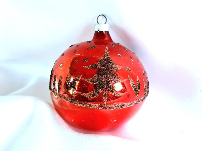 Op de afbeelding: Een rode glazen kerstbal met een gouden glitterboomontwerp.