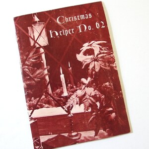 Puede incluir: Un folleto vintage de "Christmas Helper" con una portada roja que presenta una linterna, velas y vegetación. El título dice "Christmas Helper No. 62".