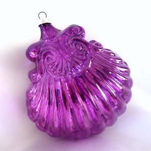 May include: A purple glass Christmas ornament shaped like a seashell with a metallic finish.