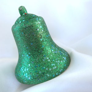 May include: A green glitter Christmas bell ornament with a loop at the top for hanging.