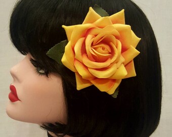 May include: A yellow and orange fabric rose hair clip. The rose is attached to a black hair clip.
