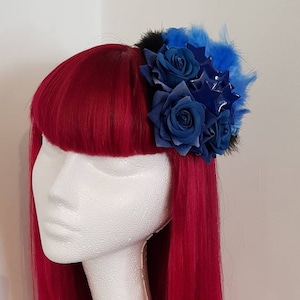 May include: A blue and black hair accessory with blue roses and star-shaped embellishments. The accessory is made of fabric and feathers.