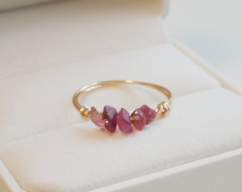 Pode incluir: Um anel de ouro com uma fileira de pedras preciosas cor-de-rosa em uma caixa de anel branca.