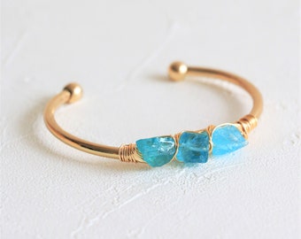 May include: A gold bangle bracelet with three blue aquamarine stones wrapped in gold wire.