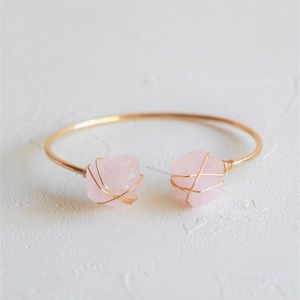 Op de afbeelding: Een gouden armband met twee roze rozenkwarts stenen.